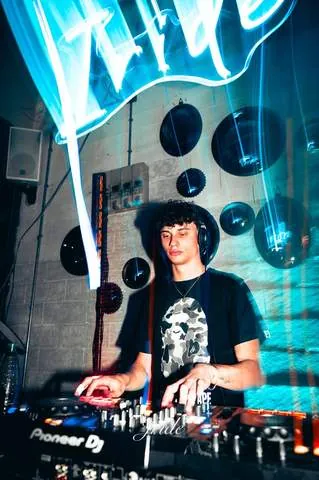 DJ con il cappello in consolle sotto l'insegna Iride